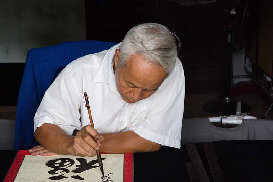Reizen door Vietnam, man maakt kalligrafie